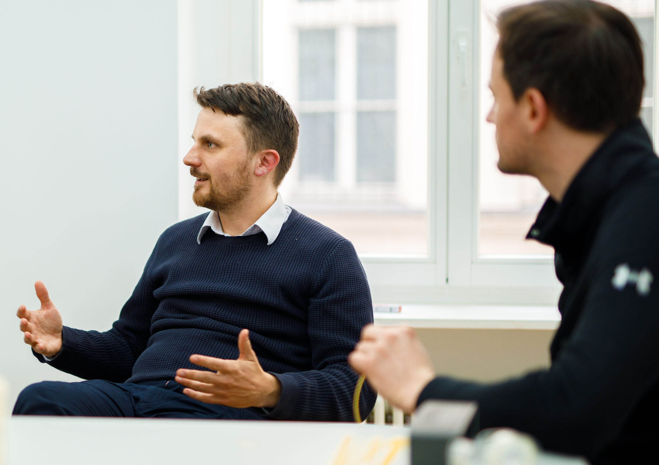 Two employees sit at a brightly lit table, deep in discussion