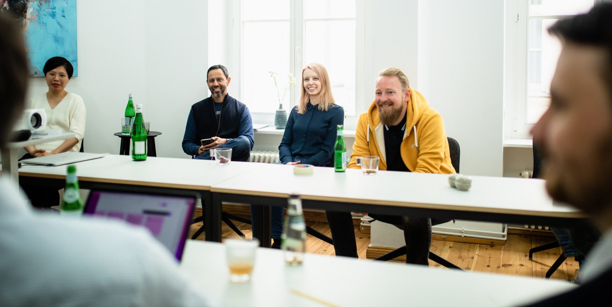 Several smiling employees sit at a brightly lit table in a meeting